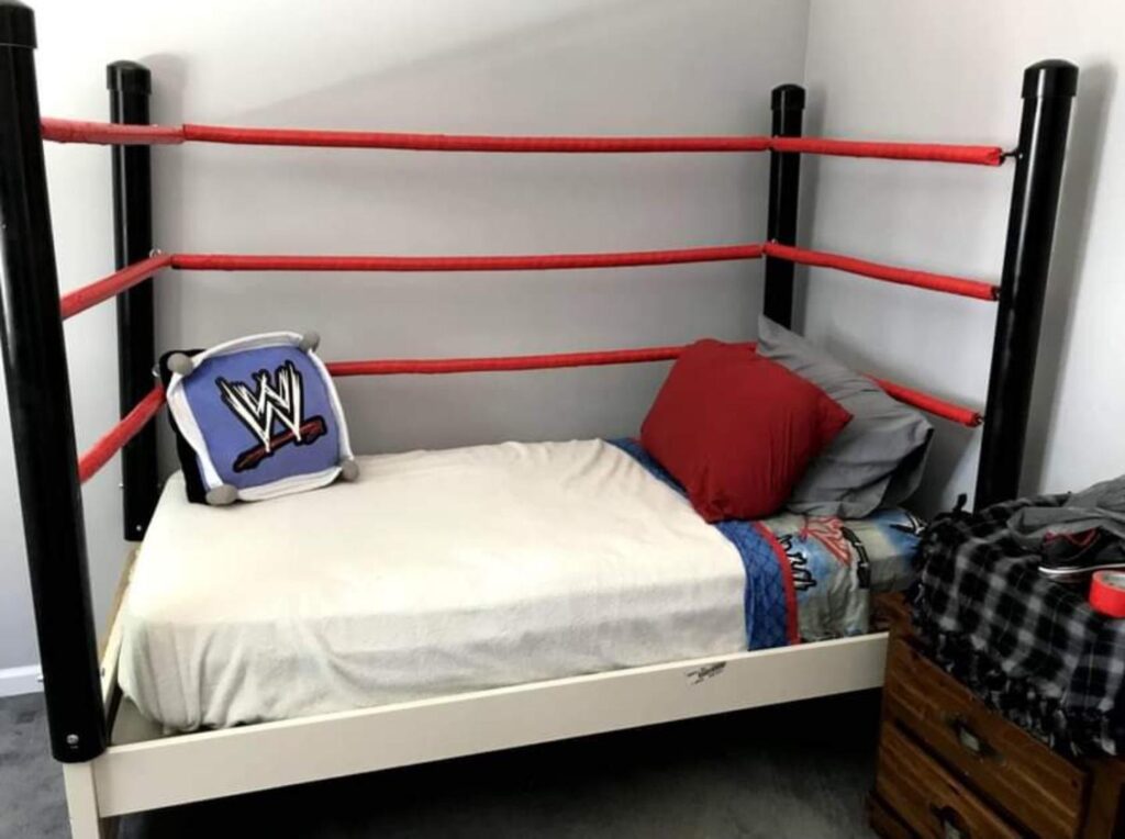 an image of a small boxing ring bed, red blue and black combination, with pillows, and wwe posters