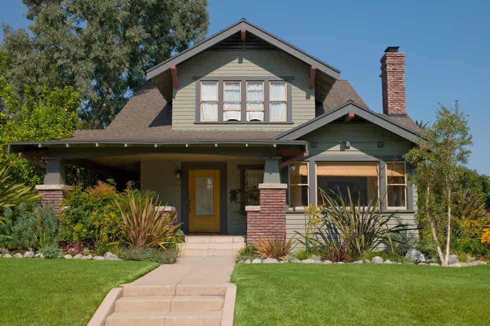 a large sage green cottage with black trims on roof, shutters, windows, and doors