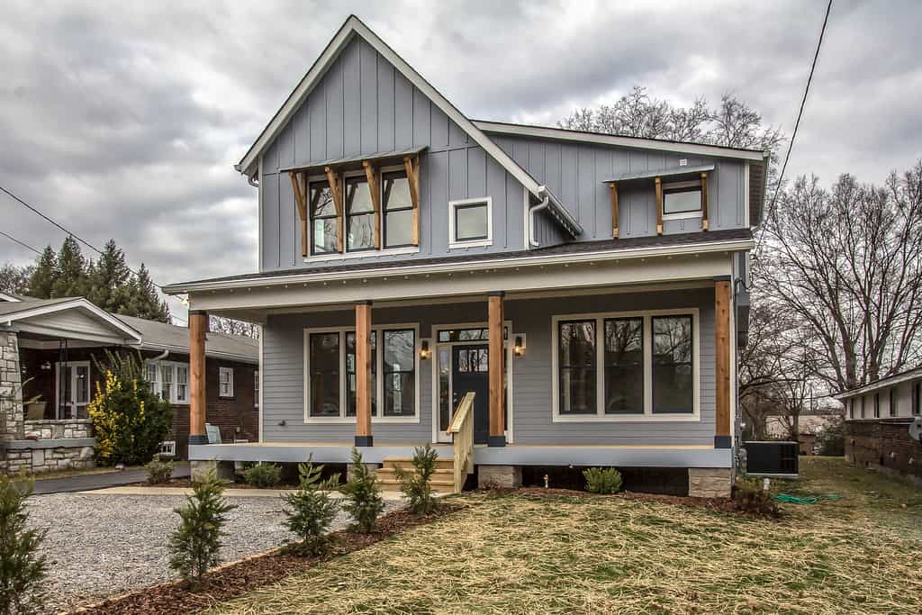a view of grey house that has some cedar accent on shutters, front door, and porch columns