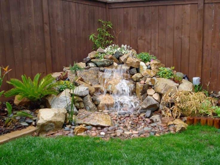 an image of a small corner garden with an fountain and rocks