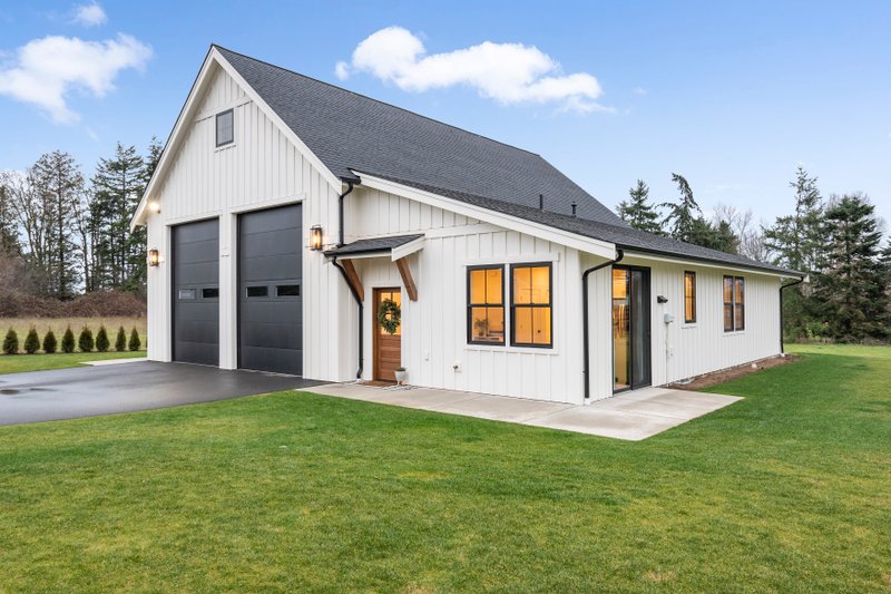 a white barndominium with black accent on garage door, window trims, and roof