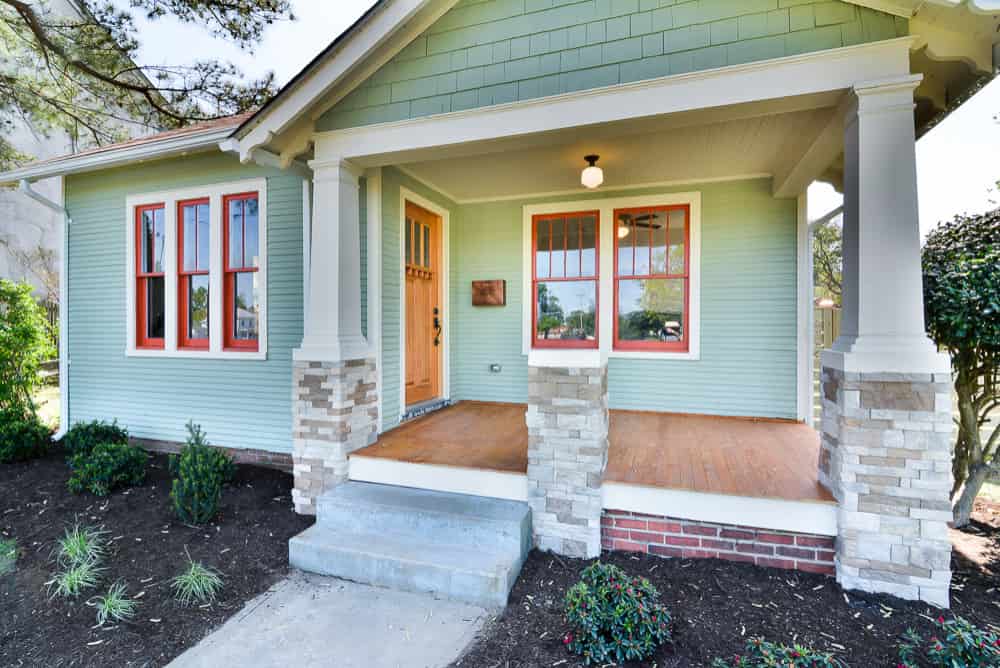 an image showing sage green house with white pillows, red window trims, and brown lighting
