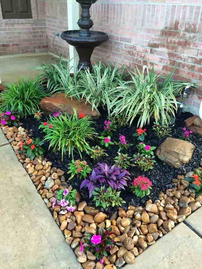 an image showing a corner garden with colorful pebble rocks with flowers and grass inside
